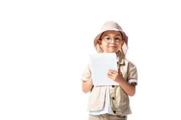 front view of cheerful explorer child in glasses and hat holding digital tablet isolated on white