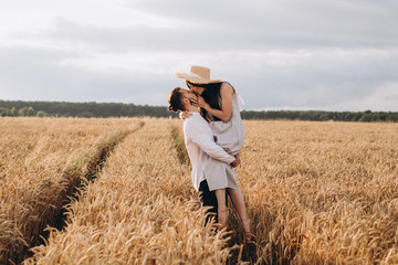 Naklejka na ściany i meble Outdoor shot of young couple walking through meadow hand in hand. Man and woman talking walk through Wheat Field in countryside. selective focus
