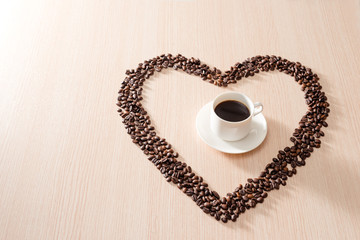 Coffee cup with roasted beans shapes love around on wood background