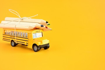 Toy school bus with pencils on the roof, back to school concept, yellow background, copy space.