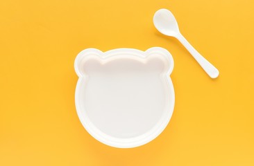 Empty plastic plate with shape of bear and white spoon on yellow background, kids eating, funny food.