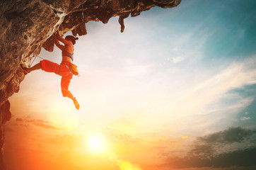 Athletic Woman climbing on overhanging cliff rock with sunset sky background.