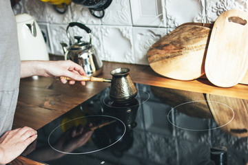 Young woman in grey dress making natural black coffee in pot in kitchen, morning routine