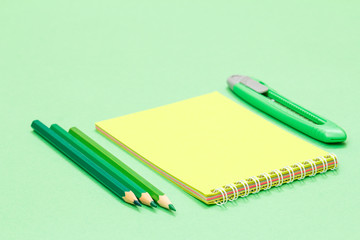 School supplies. Color pencils, notebook, and paper knife on the green background.