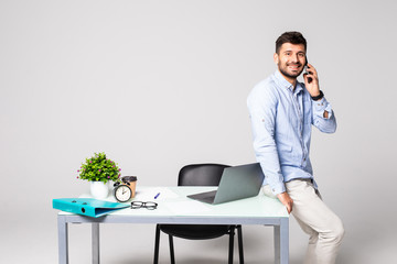 Handsome young man talking on the mobile phone and smiling while leaning at the desk in office