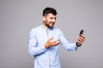 Happy smiling man watching funny video on mobile phone gadget while standing isolated on gray background