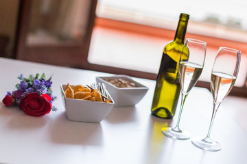 Appetizer for two. Romantic appetizer at home. Bottle of white wine, two wineglass, snacks and red rose on the table