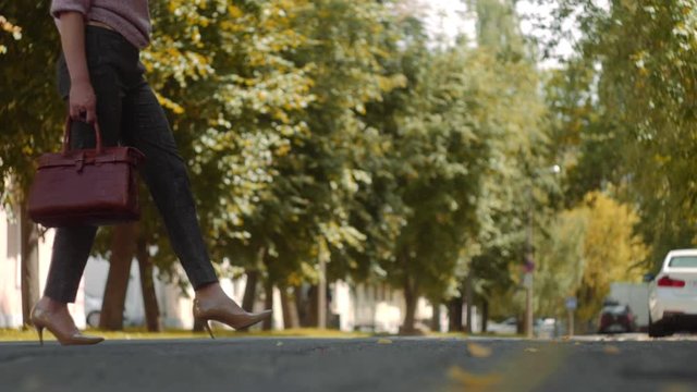 Businesswoman Legs In High-Heeled Shoes crossing the street. Female holding fation bag in her hands. Slow Motion Shot.