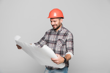 Young man construction engineer looking at blueprints while wearing helmet, isolated on white...