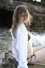 Young woman in bikini and white shirt sitting on the rocks