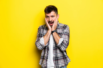 Obraz premium Portrait of scared man in panic nervous excited keeps palm on face, feals fear, isolated on yellow background. Guy shocked by scene in front of him