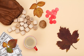 Wooden lotto barrels with bag, game cards, apple and cup of coffee on beige background. Autumn theme.