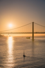 The Tejo Bridge "Ponte 25 de Abril" against golden sunlight and blue sky in Lisbon, Portugal 