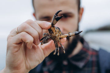 Portrait of a stylish bearded man with a small crab in his hands during the first tour of the sea