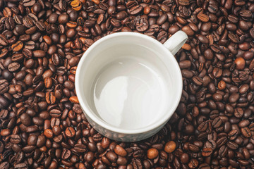 empty white mug on a background of coffee beans, top view, copy space