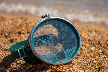 A mask for swimming under water lies on the sandy shore.