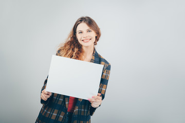 Caucasian girl holding a blank canvas in her hands and smiling, grey wall on background. Copy...