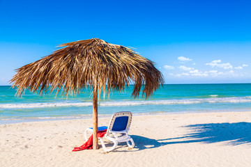 A sun lounger under an umbrella on the sandy beach by the sea and sky. Vacation background. Idyllic beach landscape.