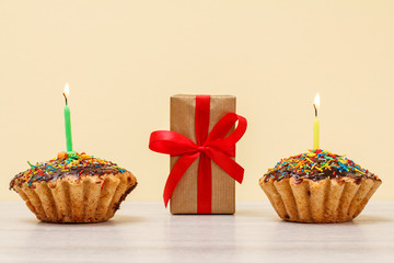 Tasty birthday muffins with burning festive candles and gift box on beige background.