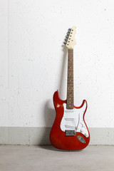 Fototapeta na wymiar Red electric guitar standing against white raw wall