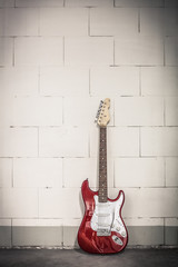 Fototapeta na wymiar Red electric guitar stands against white brick wall background, toned crisp vignette image