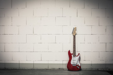 Fototapeta na wymiar Red electric guitar stands to the right against white brick wall, toned crisp vignette image