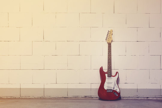 Red electric guitar stands to the right against white brick wall, yellow magenta toned image