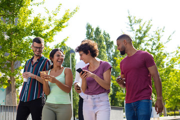 Happy joyful friends with smartphones discussing funny news. Men and women walking together outside, using mobile phones, chatting and laughing. Gadgets using concept