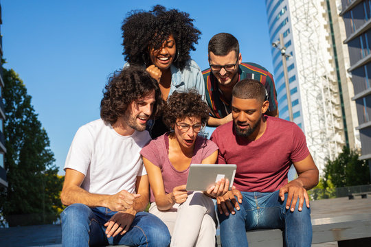 Excited Happy People Watching Sport Match On Tablet Outdoors. Team Of Friends Sitting Outside, Using Tablet, Staring At Screen And Shouting. Sport Fans Or Bet Concept