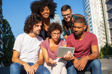 Puzzled woman using tablet outdoors. Her joyful happy friends staring on screen. Communication or video call concept