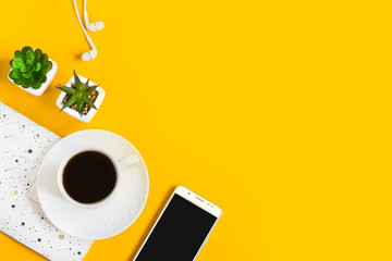 Morning coffee, notebook, mobile phone, plants on a yellow background. Copy space. Top view....