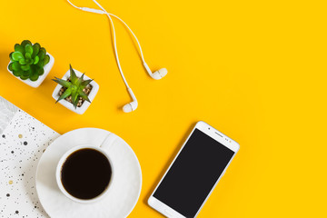 Morning coffee, notebook, mobile phone, plants on a yellow background. Copy space. Top view....