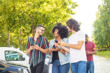 Interracial team of three walking outside with smartphones. Happy friends chatting, discussing news, using mobile phones. Communication concept