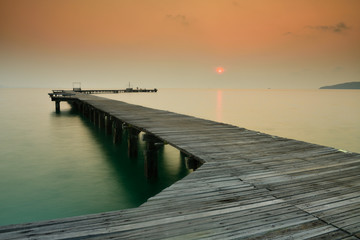 Obraz premium Wooden bridge that stretches into the sea at sunrise.