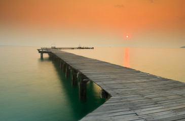 Fototapeta na wymiar Wooden bridge that stretches into the sea at sunrise.