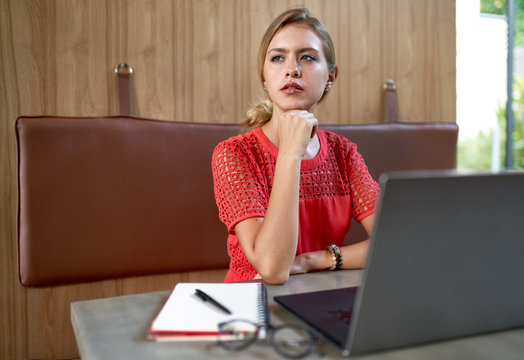 Closeup lifestyle portrait of young concentrated blonde caucasian millennial fashion designer working in a bright modern restaurant wearing bright clothing