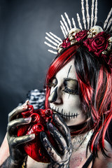 Woman with sugar skull makeup holding a bloody heart