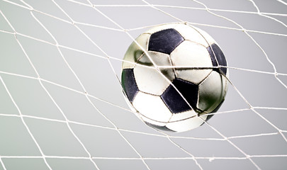 Naklejka premium Scoring goal, Soccer ball in the net against gray background.