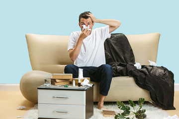 Young man suffering from hausehold dust or seasonal allergy and headache. Sneezing in the napkin,...