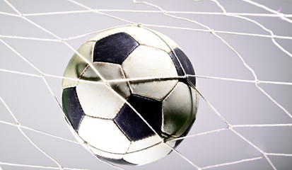 Naklejka premium Scoring goal, Soccer ball in the net against gray background.