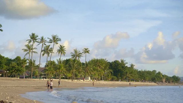 Group of young people is walking, playing and taking photos in sunset beach in Bali island
