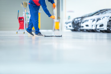 Car mechanic repair service center cleaning using mops to roll water from the epoxy floor. In the...