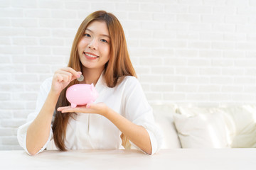 Obraz na płótnie Canvas hand putting coin money to piggy bank saving, Close up of woman smiling putting a coin inside piggy bank as investment