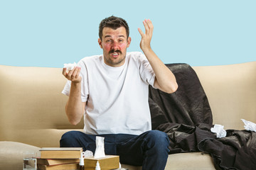 Young man suffering from hausehold dust or seasonal allergy. Sneezing in the napkin and sitting...