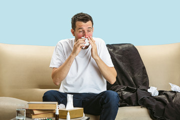 Young man suffering from hausehold dust or seasonal allergy. Sneezing in the napkin and sitting...