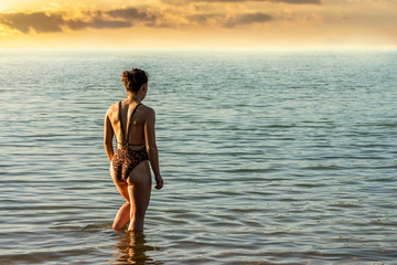 Beautiful woman in a bikini goes into the water at sunset