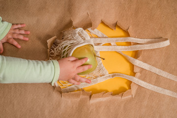 Fresh fruit in a string bag. Orange, lemon and I are blocky. Ecological packaging. Hole in craft background, torn craft yellow paper. Zero waste concept. copy space, flat lay. baby hand takes fruit.