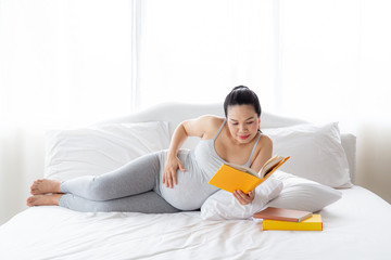 Pregnancy and motherhood concept - Happy pregnant woman reading book on white bed.