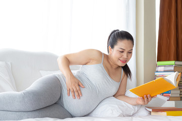 Pregnancy and motherhood concept - Happy pregnant woman reading book on white bed.