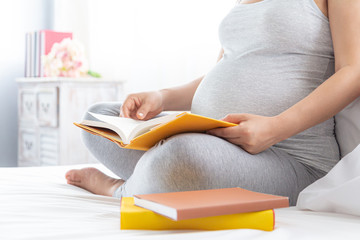 Pregnancy and motherhood concept - Happy pregnant woman reading book on white bed.
